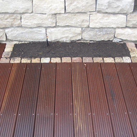 Rotbraune Holzdielen einer Terrasse mit Einfassung aus hellen Pflastersteinen
