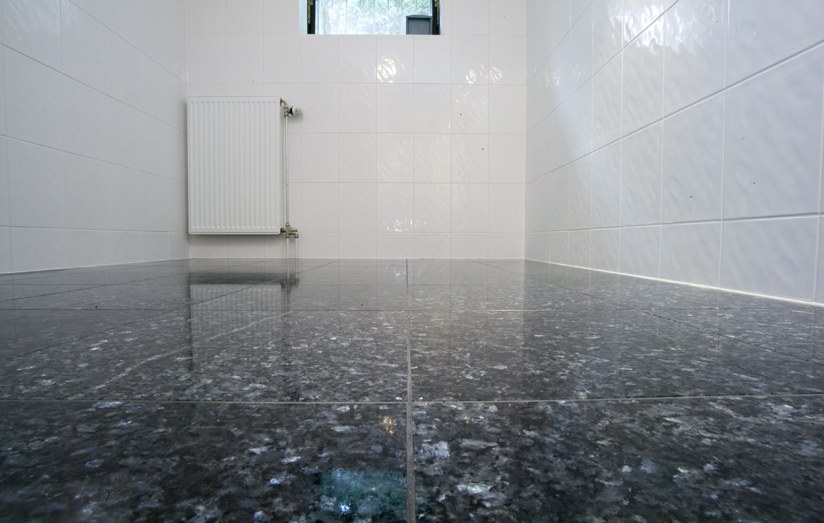 Kellerboden aus polierten Natursteinfliesen Blue Pearl, dahinter weiße Wände und Heizkörper