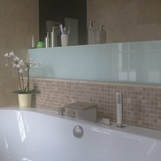 Badewanne vor Wand mit hellen Natursteinfliesen und Mosaikband